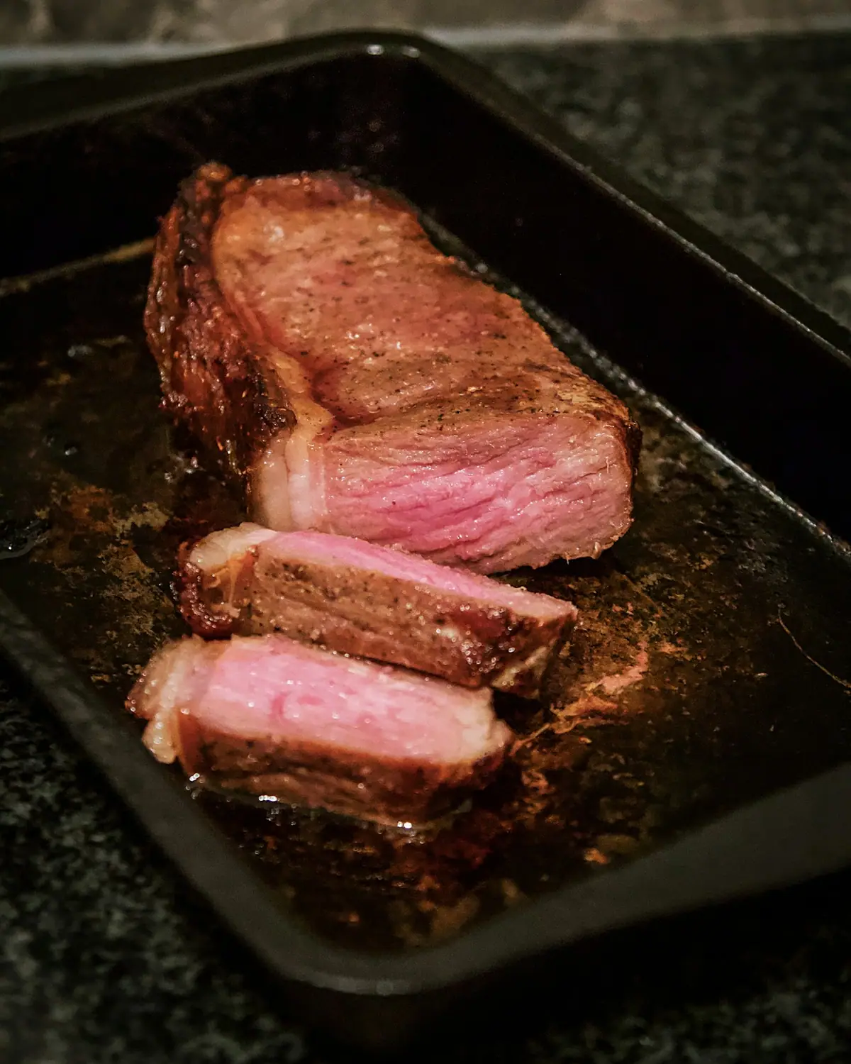 Thick slices of rosy roast beef on a dark tray