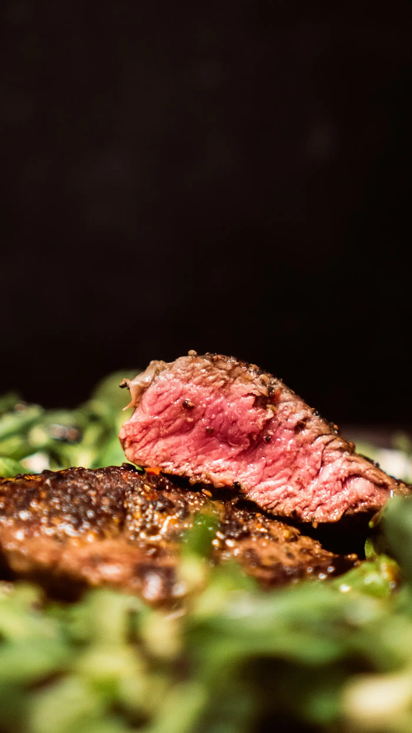 A seared steak with a pink centre resting on greens