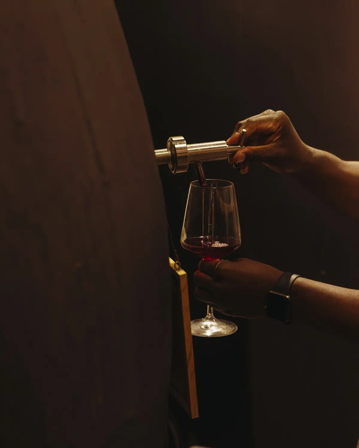 A hand holding a glass of red wine in low light